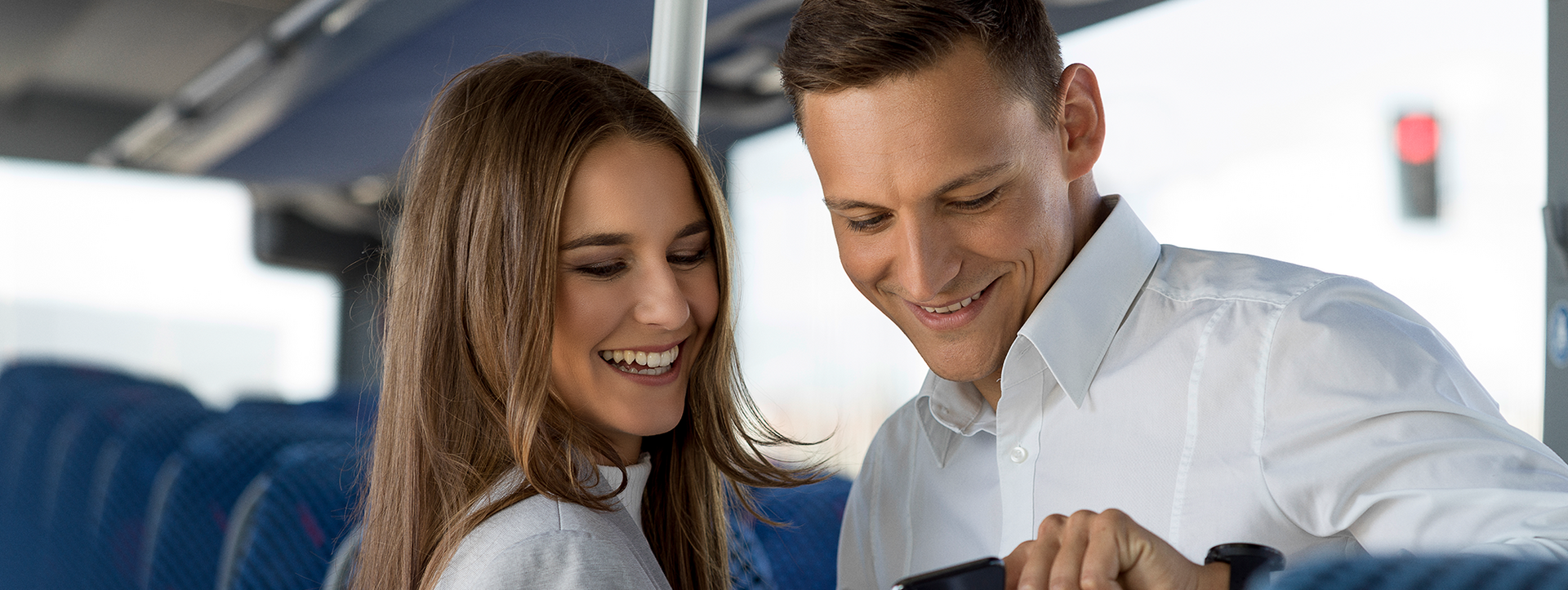 OÖVV Regionalbus Fahrgäste Ein Mann und eine Frau in einem Bus schauen lächelnd auf ein Smartphone.