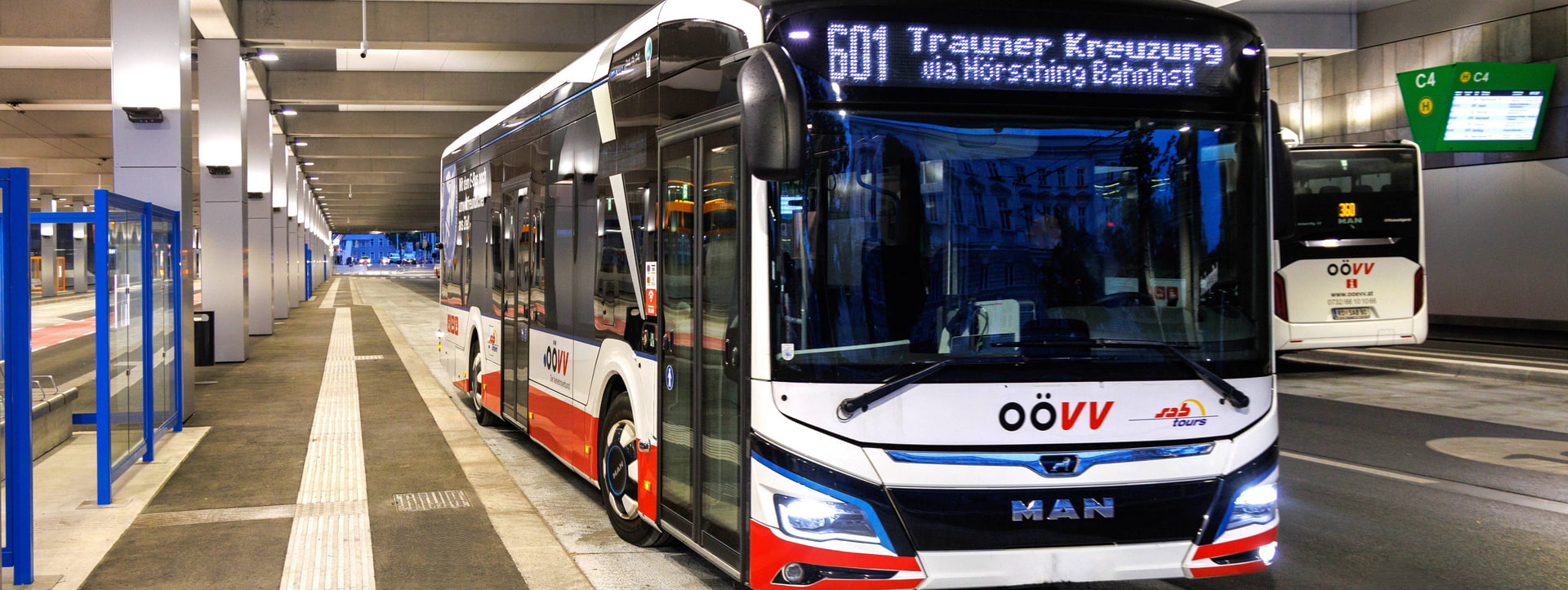 A modern city bus in front of a bus station, with more buses in the background.
