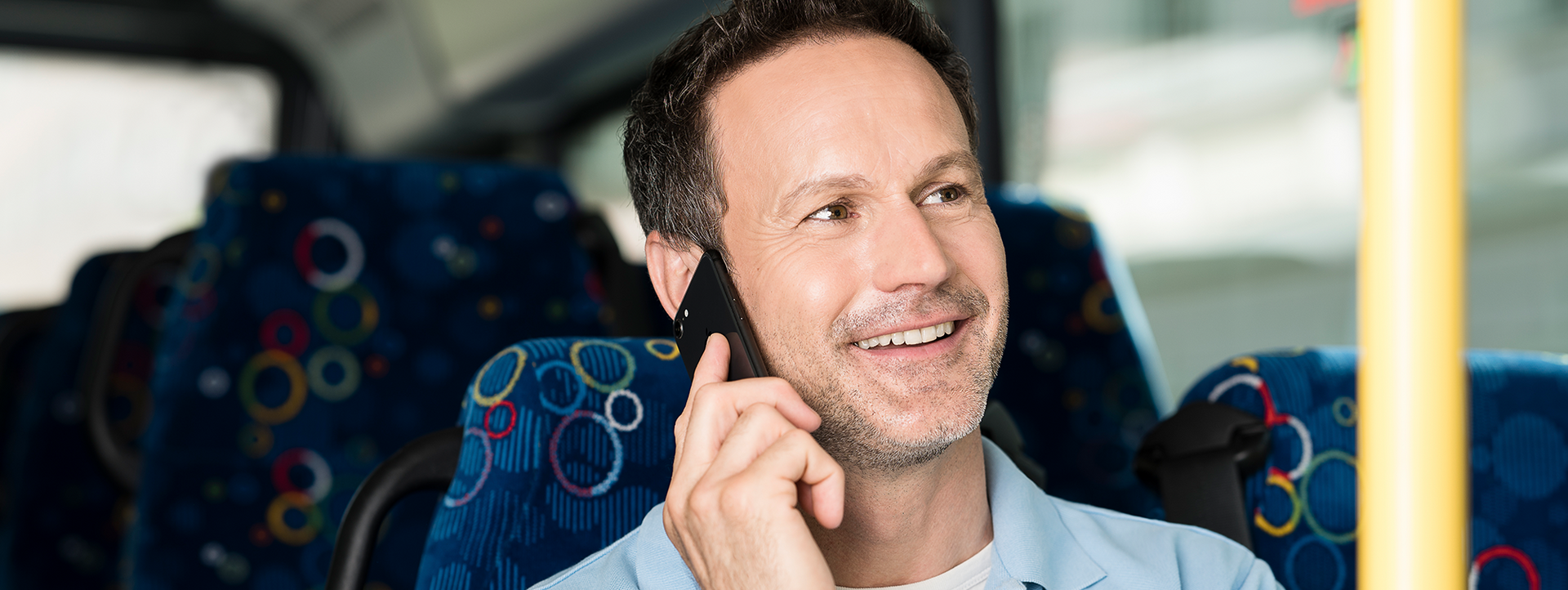 Smiling man on a bus talks on his cellphone.